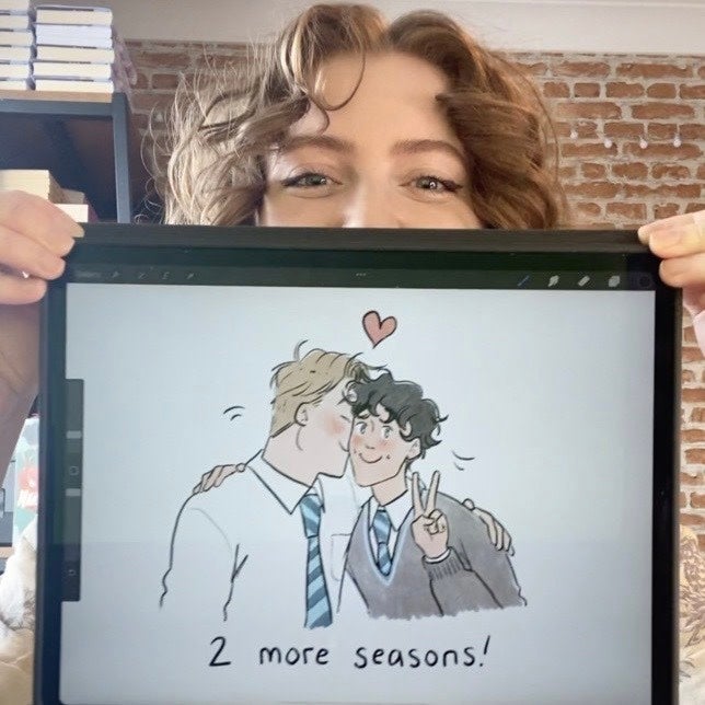 Alice Oseman holds up tablet with a drawing of Nick and Charlie that reads "Two more seasons!" Image from Netflix