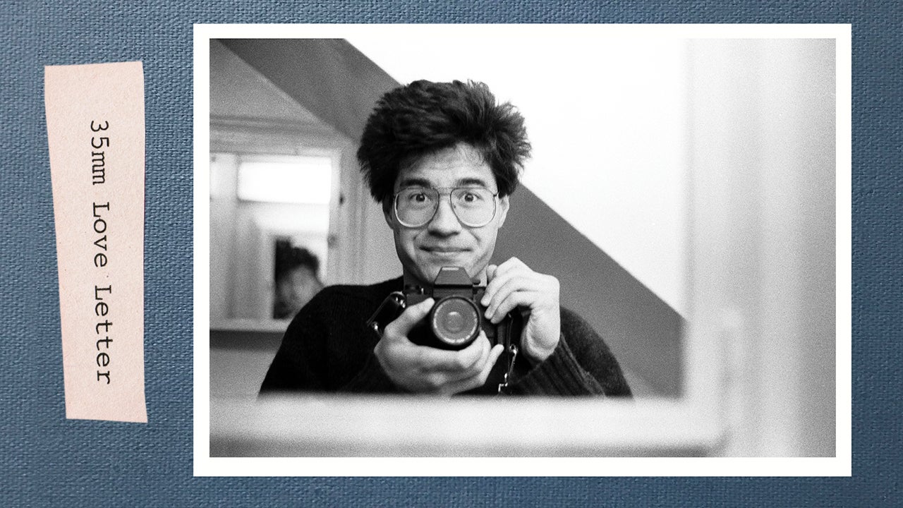 A black and white photo of Greg Pak taking a self portrait in a mirror on a blue background