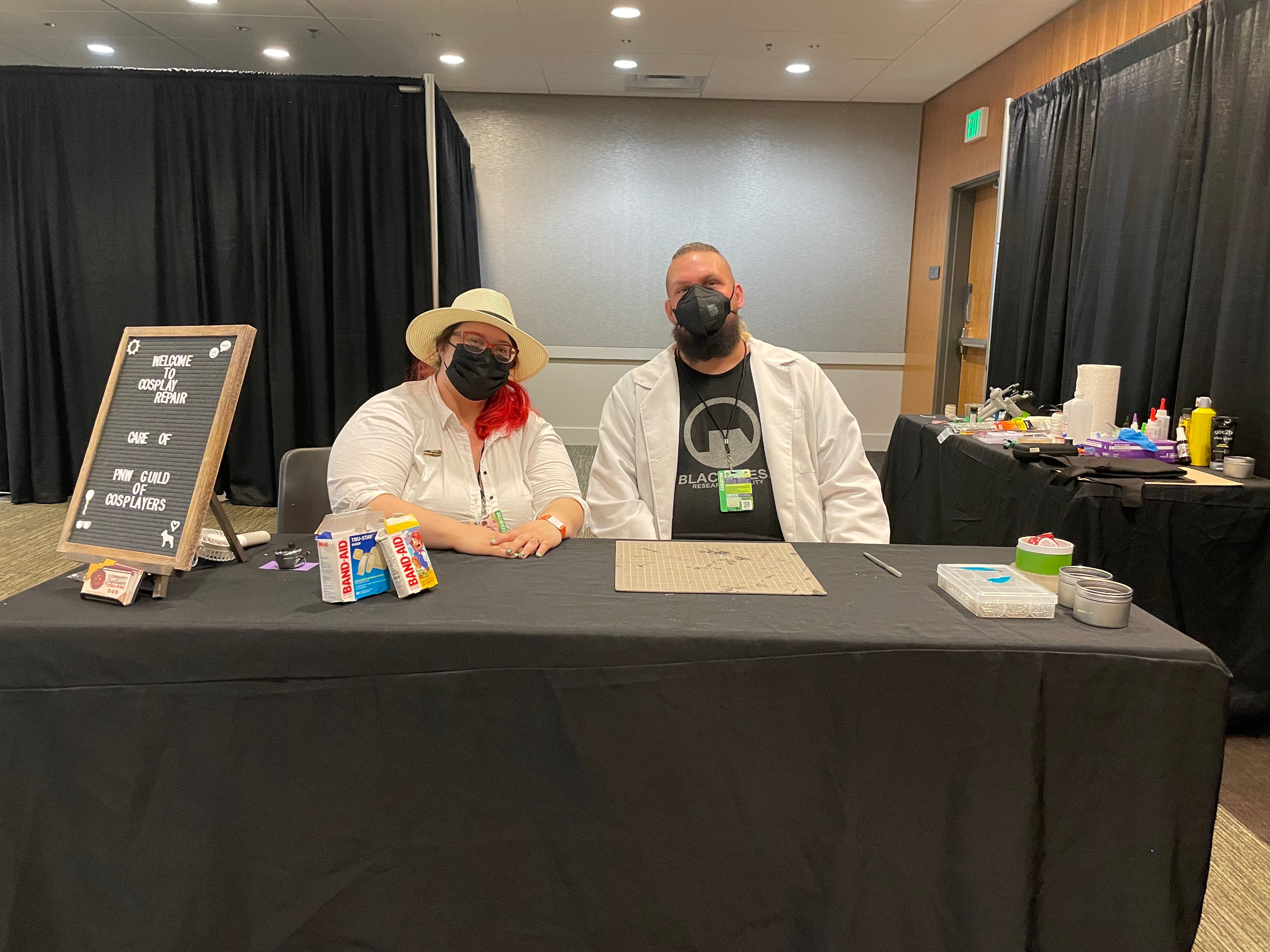 Jessica Mcgee and Bryce Mcgee sitting at the cosplay repair table with supplies behind them