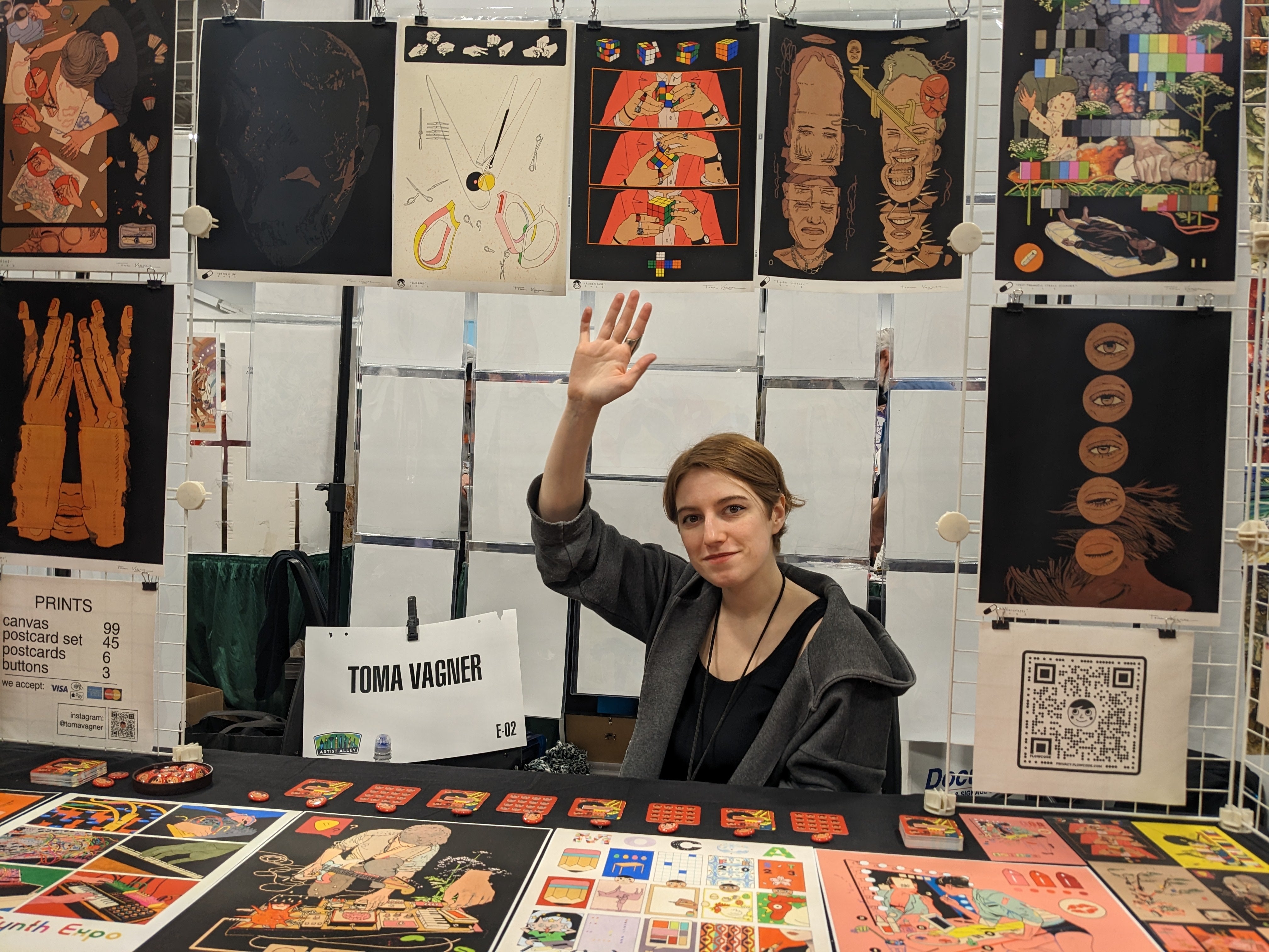Photograph of artist in her booth with her hand raised