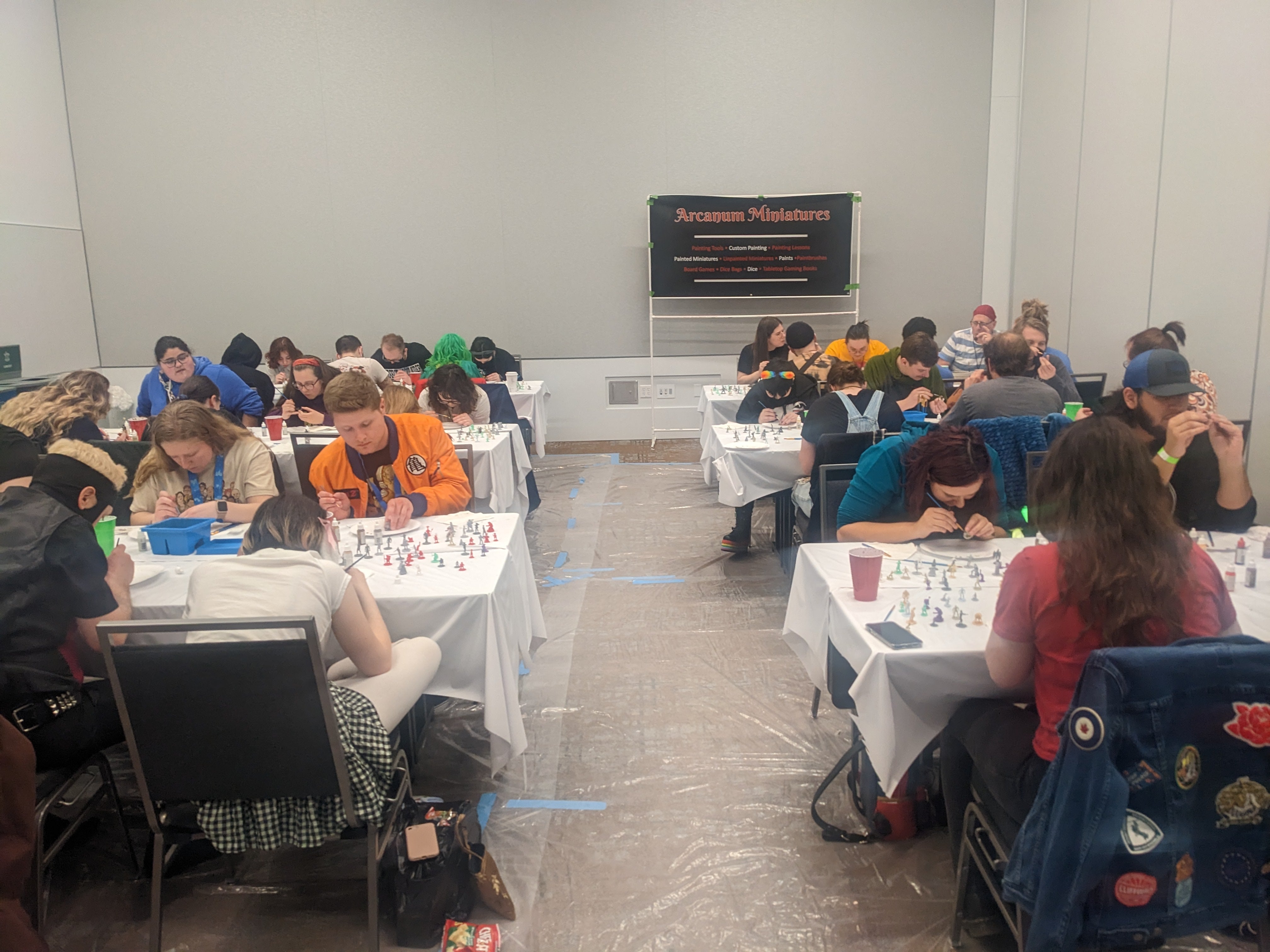 Photograph of fans sitting in a room at tables painting miniatures