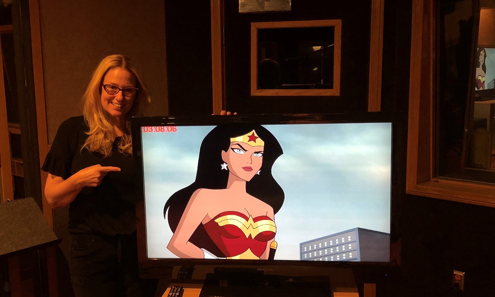 Voice actor Susan Eisenberg standing next to a TV with an image of Wonder Woman, a superhero, standing