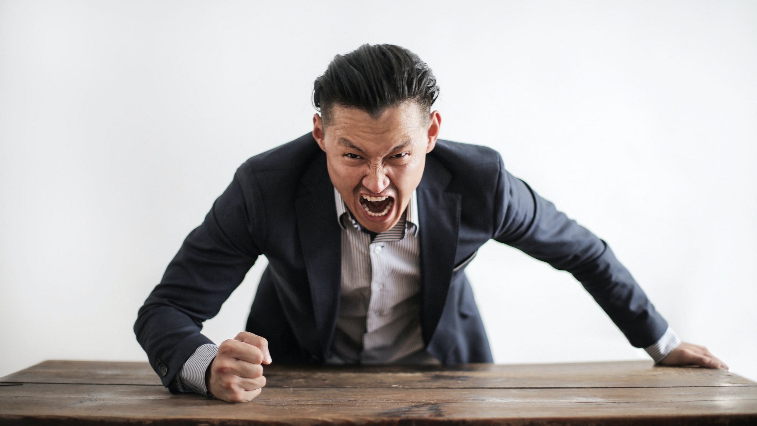 A screaming man in a suit bangs a desk