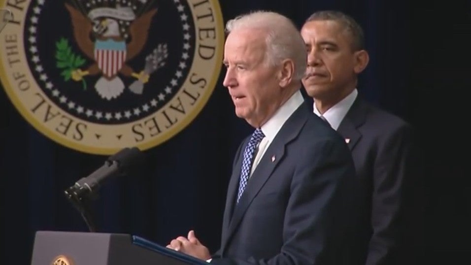 Joe Biden speaks with Barack Obama in the background at a January 2013 White House press conference on the administration's response to the Sandy Hook Elementary School shooting