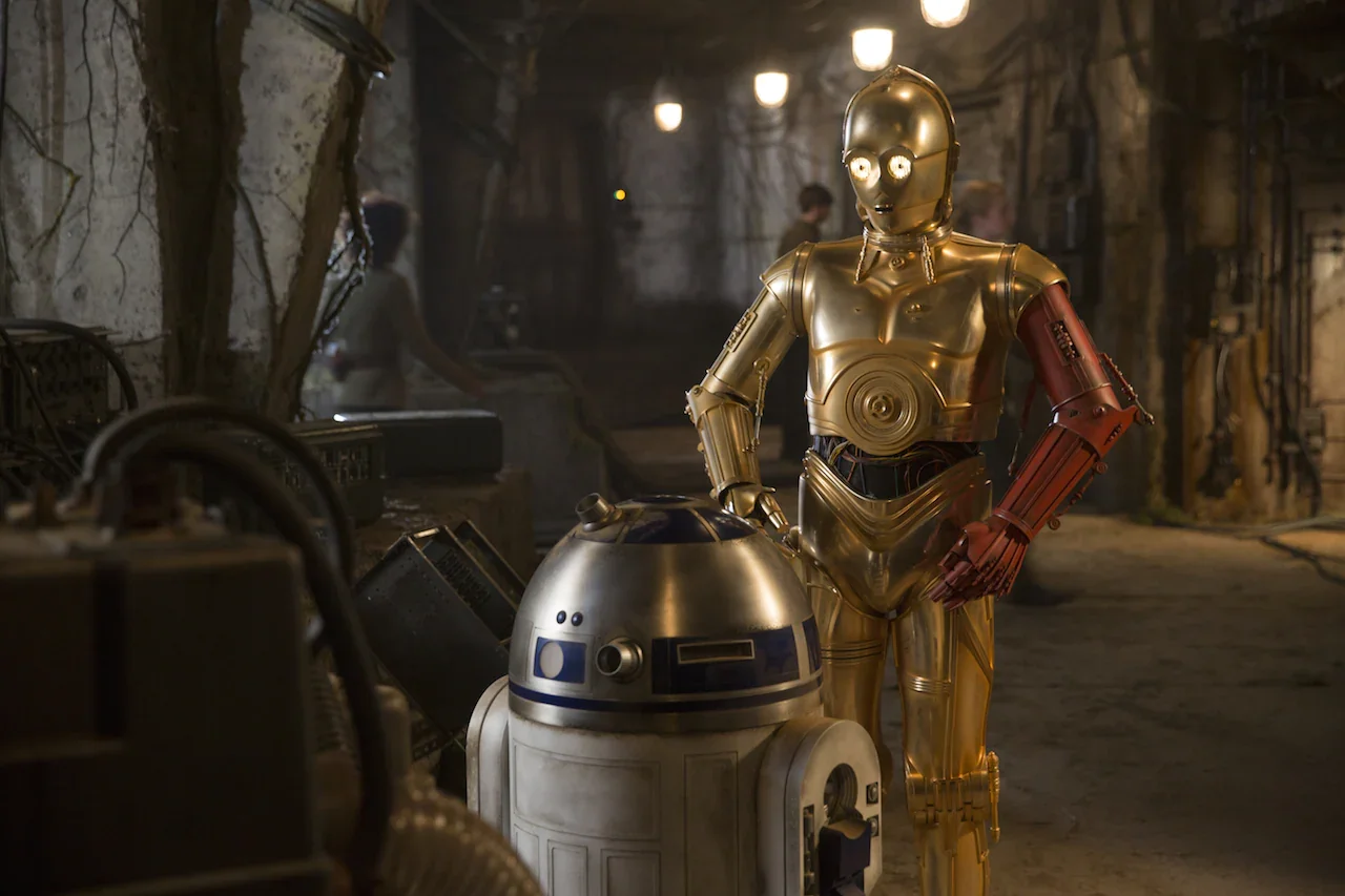 Still image from The Force Awakens. A red-armed C-3P0 and R2-D2 facing each other