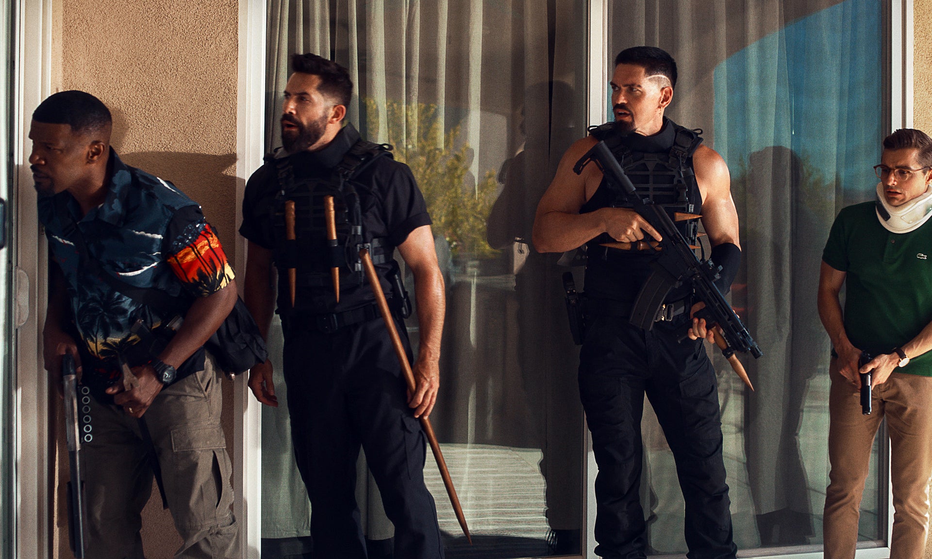 A still image of four men looking to the left, outside of an apartment, holding weapons