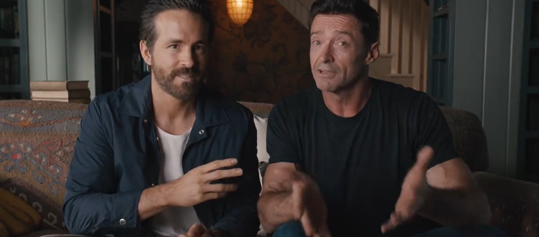 Ryan Reynolds and Hugh Jackman sitting side by side on a couch