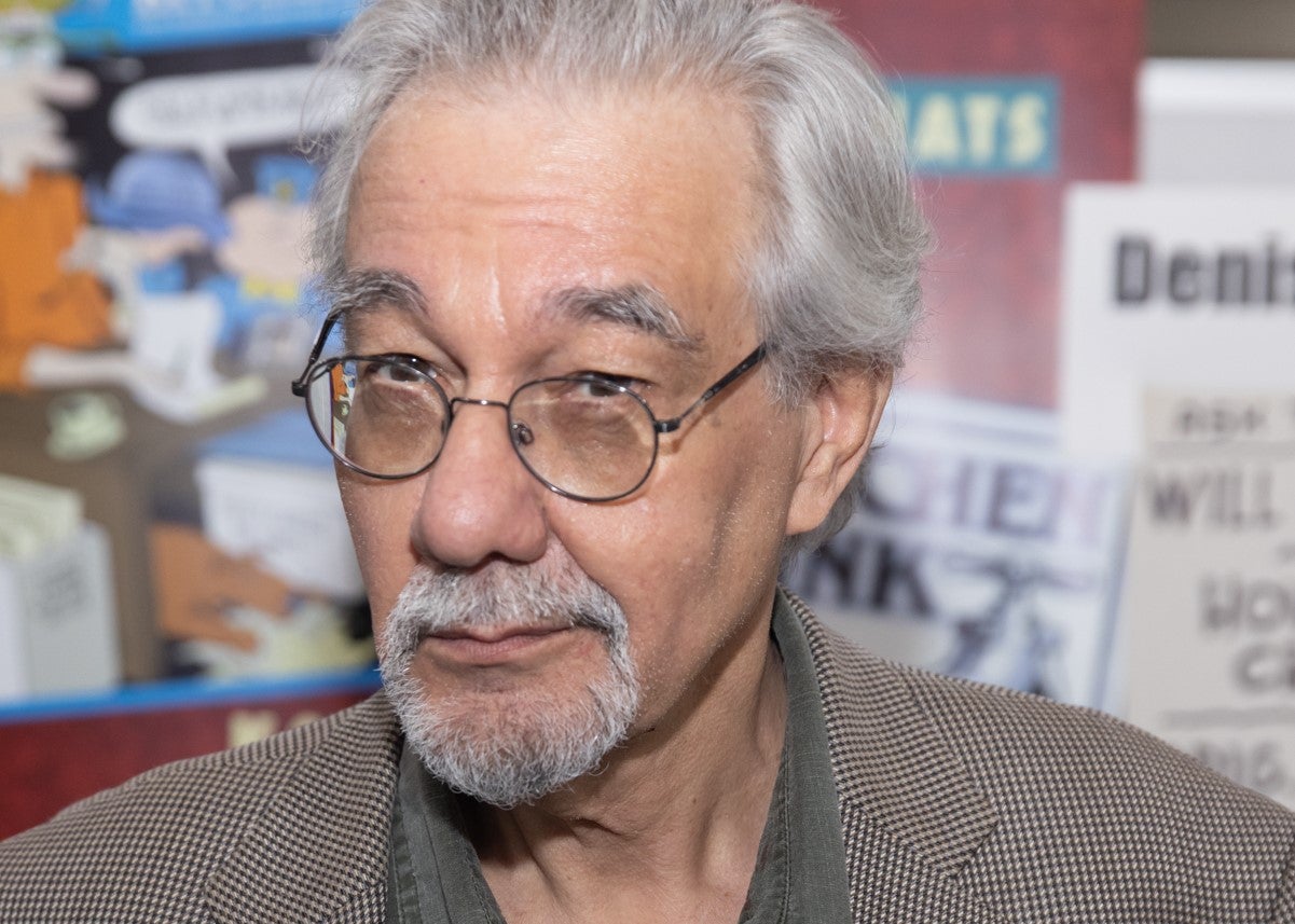 Photograph of Denis Kitchen wearing glasses and a brown blazer in front of his Artists Alley table