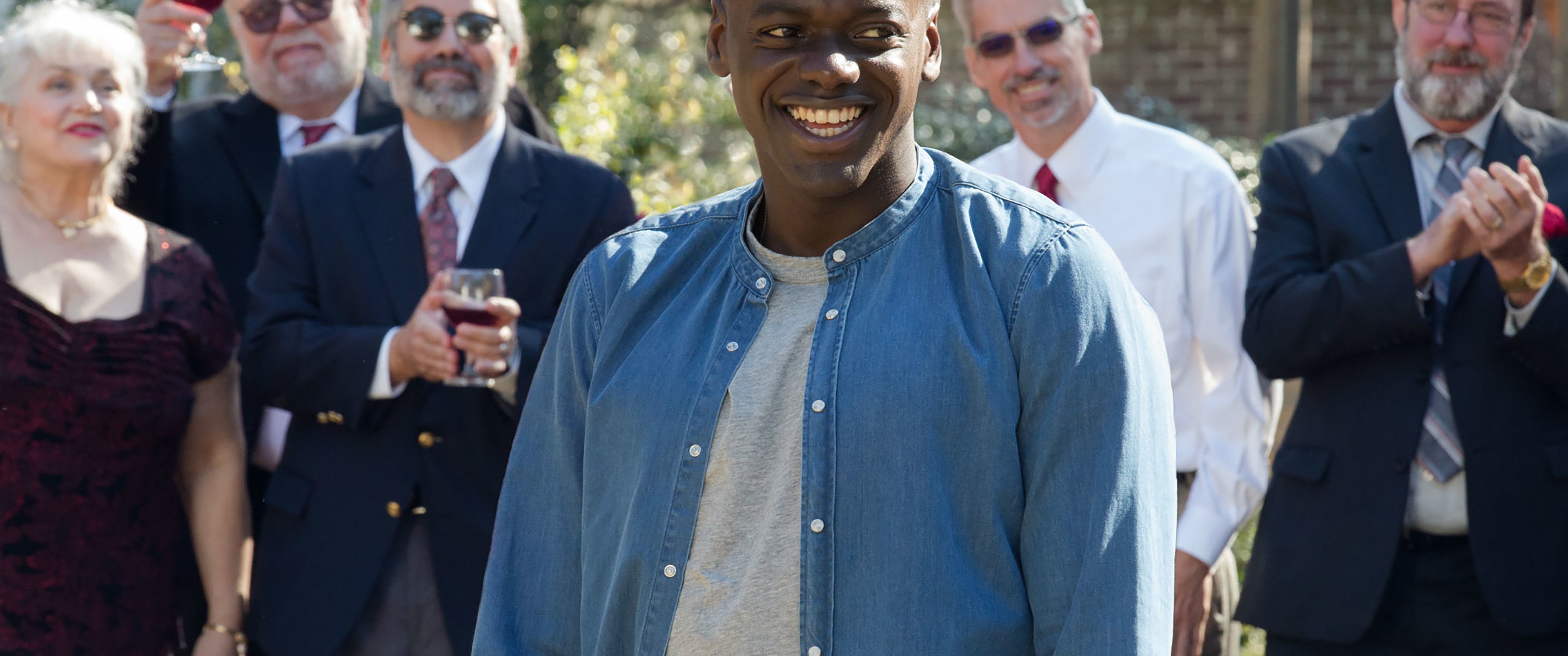 Still image from Get Out. Daniel Kaluuya smiling amongst but separate from partygoers.