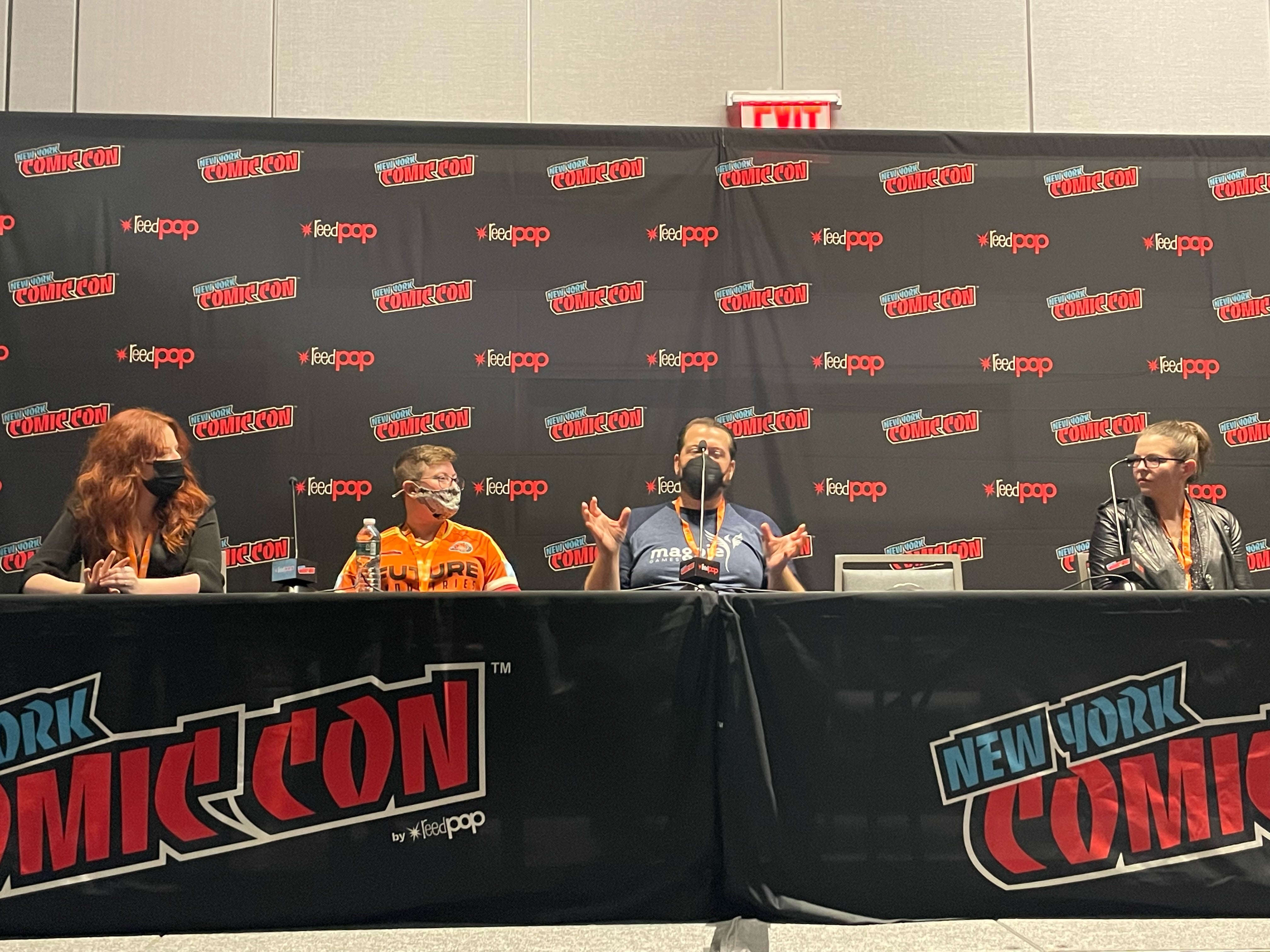 Panelists sitting in front of microphones in front of a NYCC background