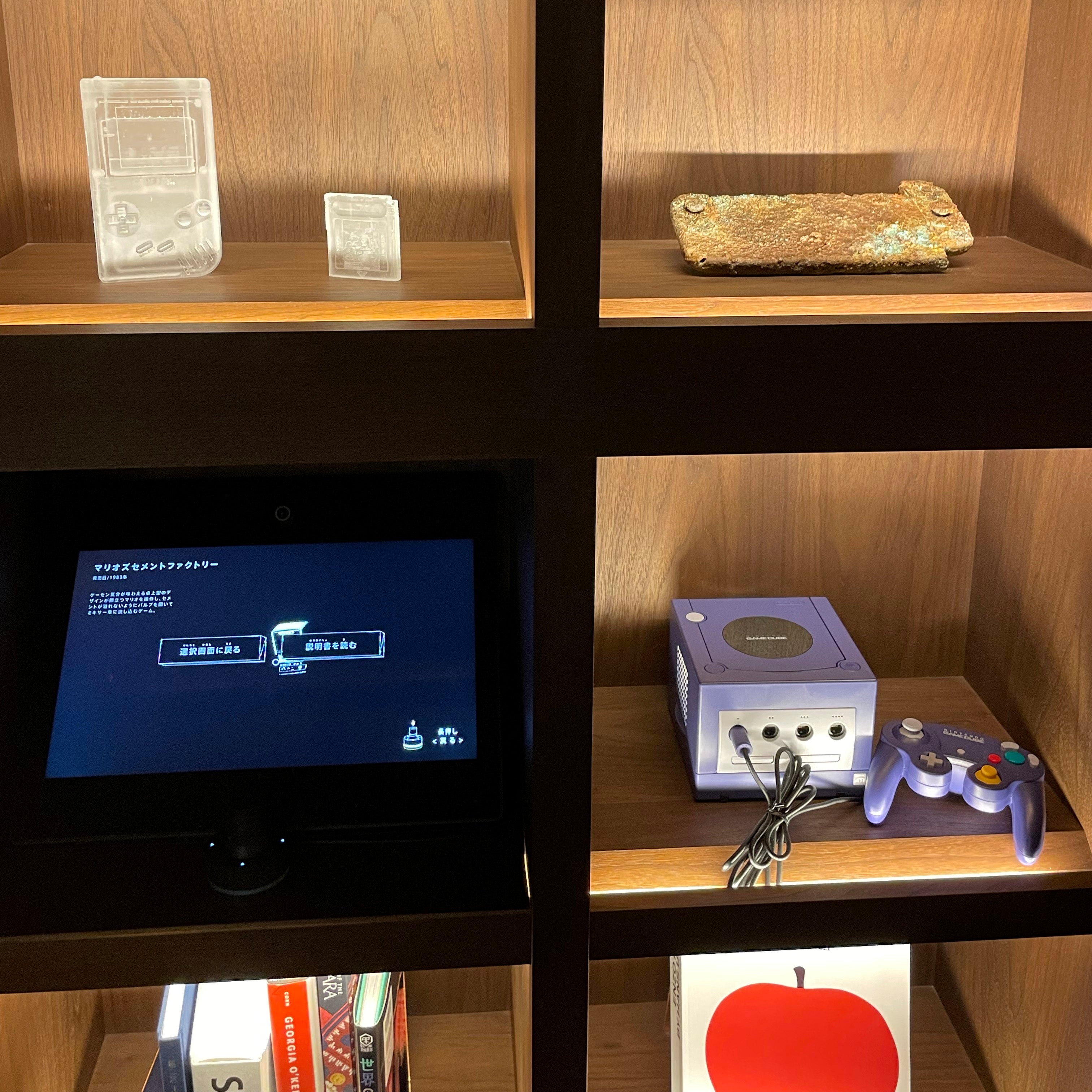 Une étagère avec ce qui ressemble à une Nintendo Switch incrustée d'or et une autre avec un GameCube à l'intérieur.