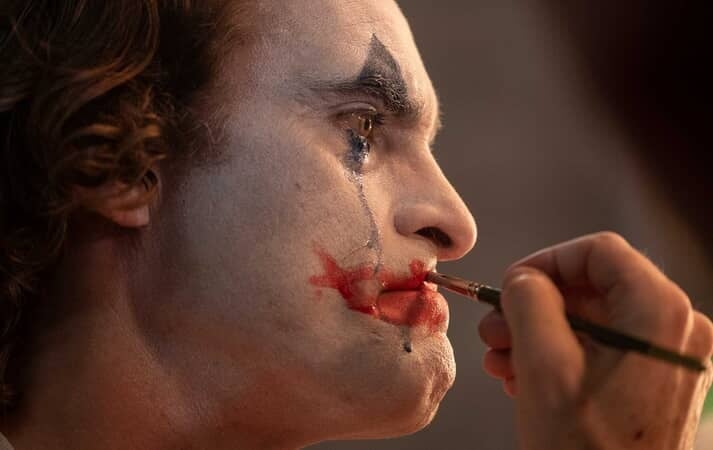 Image of Joaquin Phoenix as the Joker putting on clown makeup