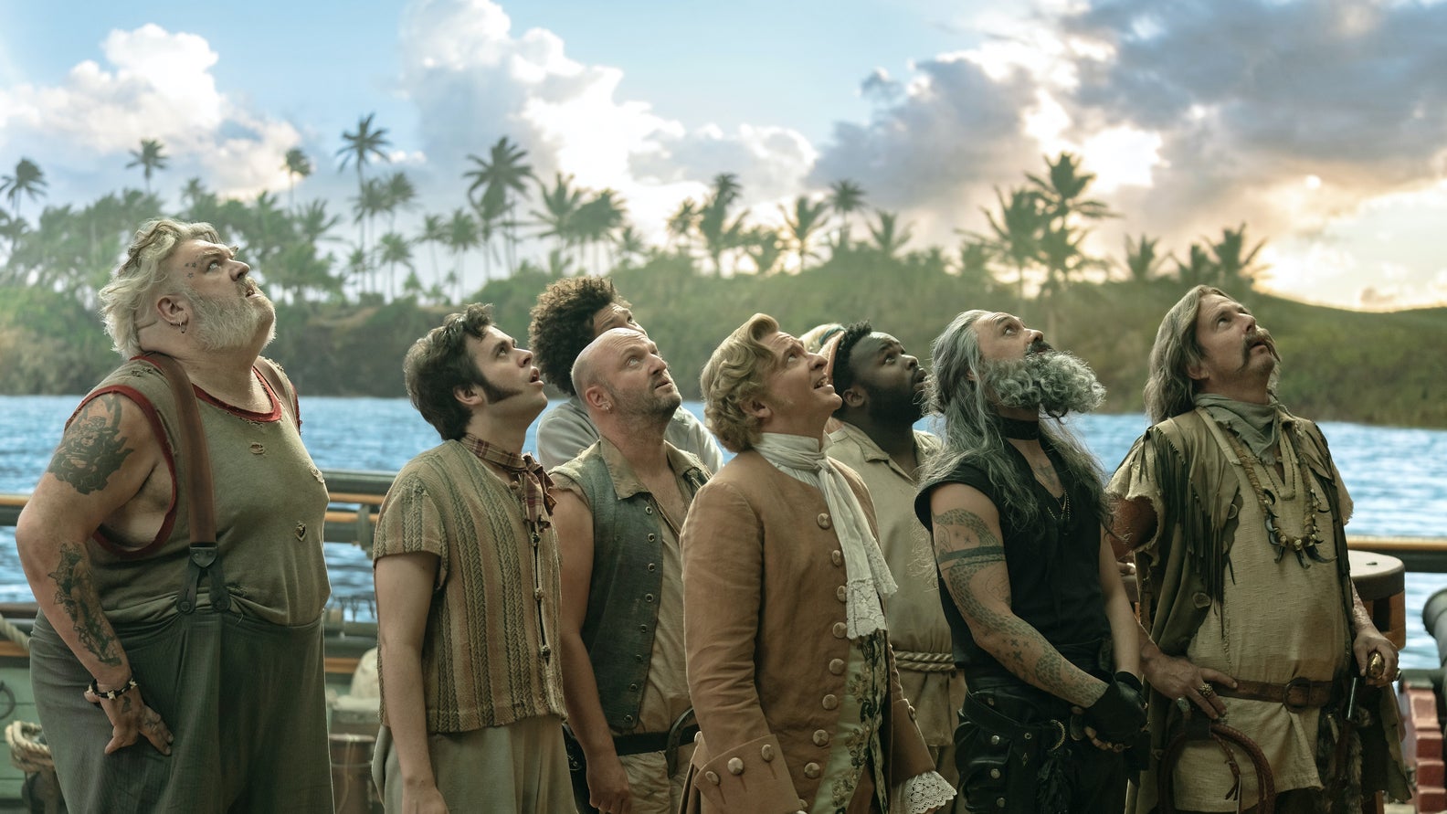 Photograph of a group of pirates on a ship with the sea behind them, looking up at the sky