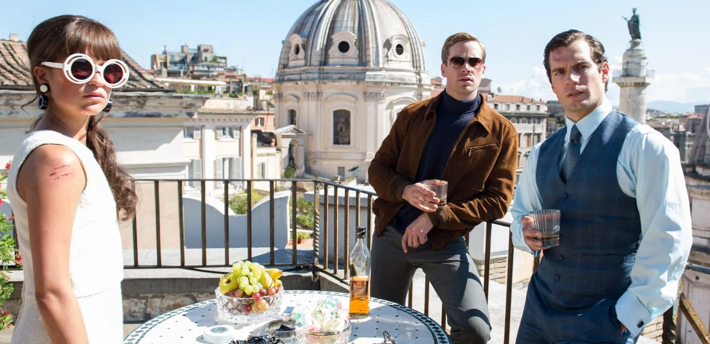 Still image of Alicia Vikander, Armie Hammer, and Henry Cavill standing on a balcony