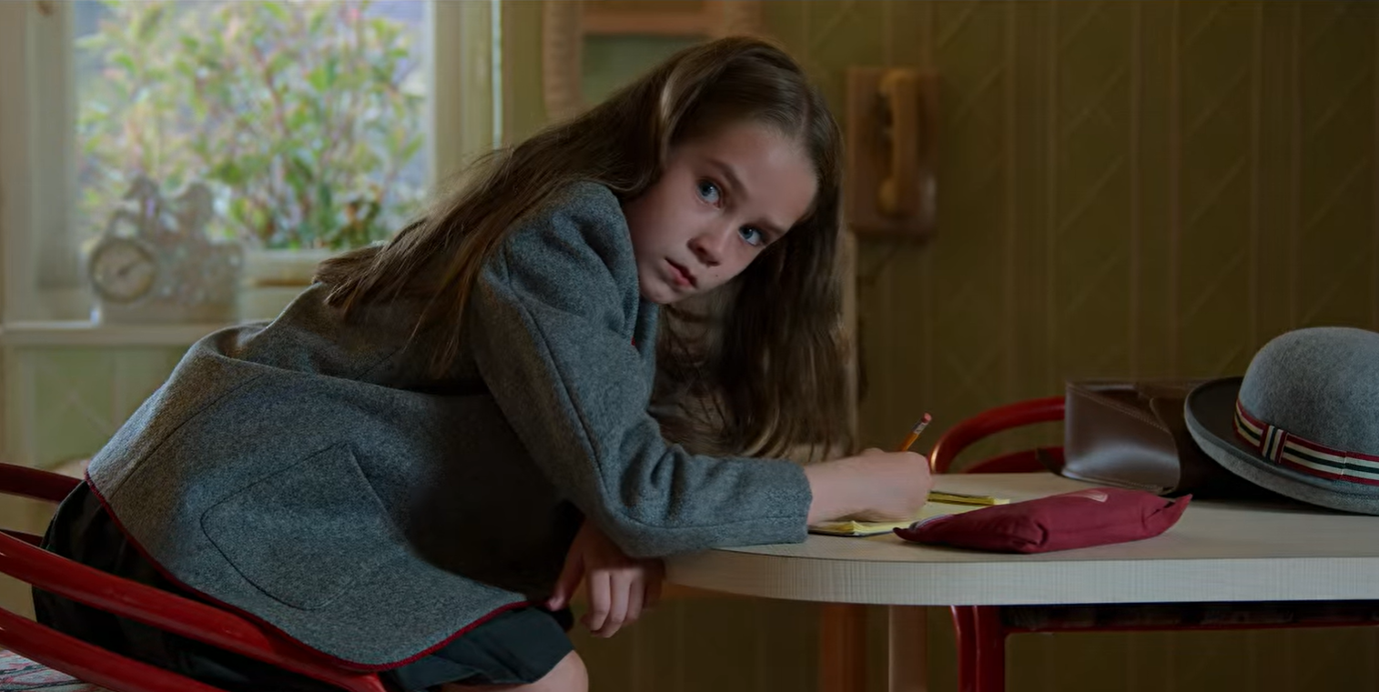 Still image of Matilda reading at a table wearing her school uniform