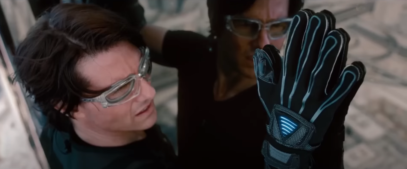 Still image of Tom Cruise as Ethan Hunt wearing goggles and gloves, holding onto the exterior of a skyscraper