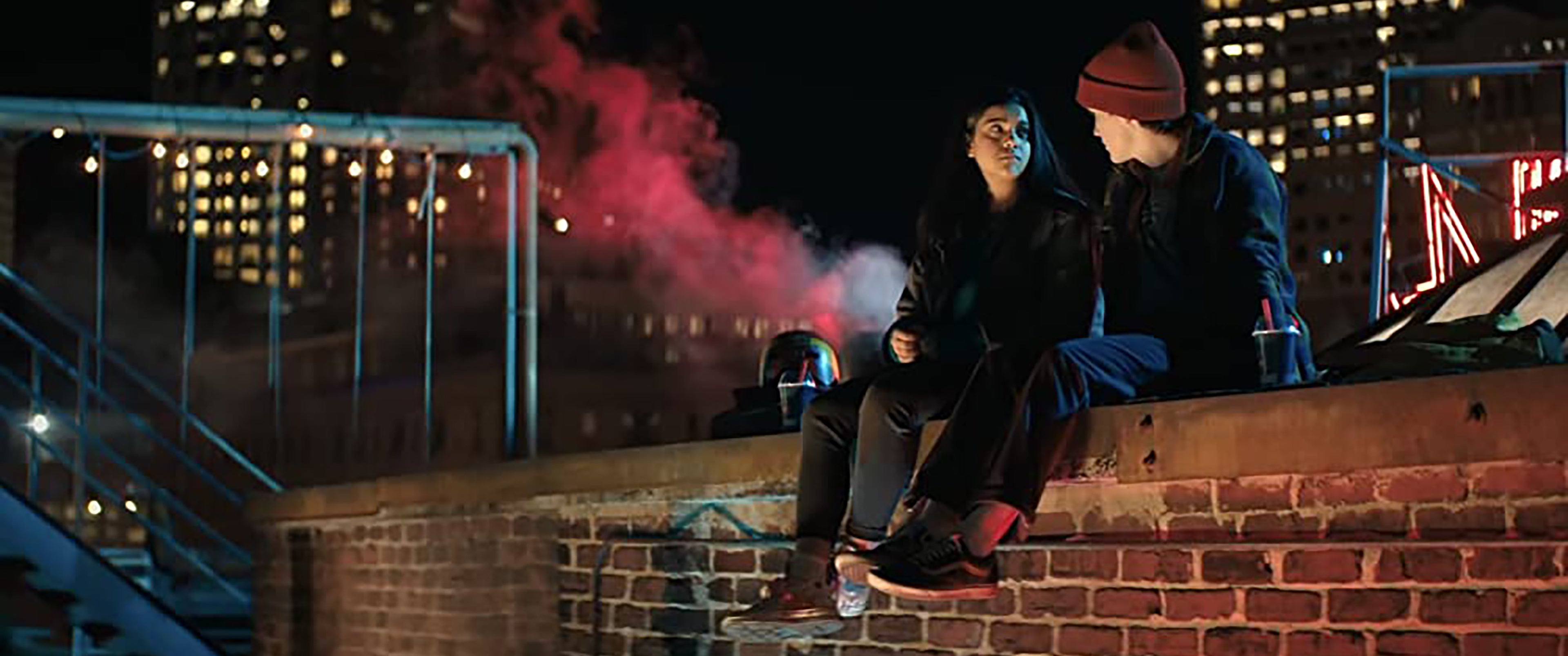 Ms. Marvel still Iman Vellani as Kamala Khan sitting on a rooftop at night with Matt Lintz as Bruno Carrelli