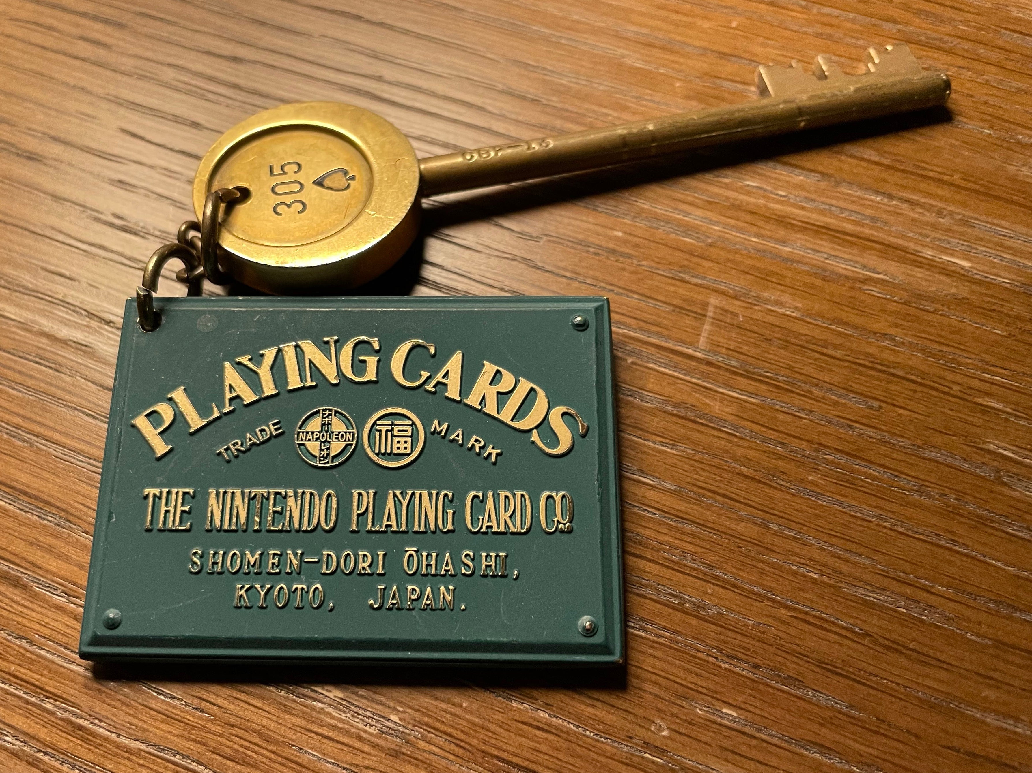 A Mortis key with a number on it, attached on a keyring to a green, card-sized rectangular metal plaque that reads "Playing Cards" by "The Nintendo Playing Card Co.".