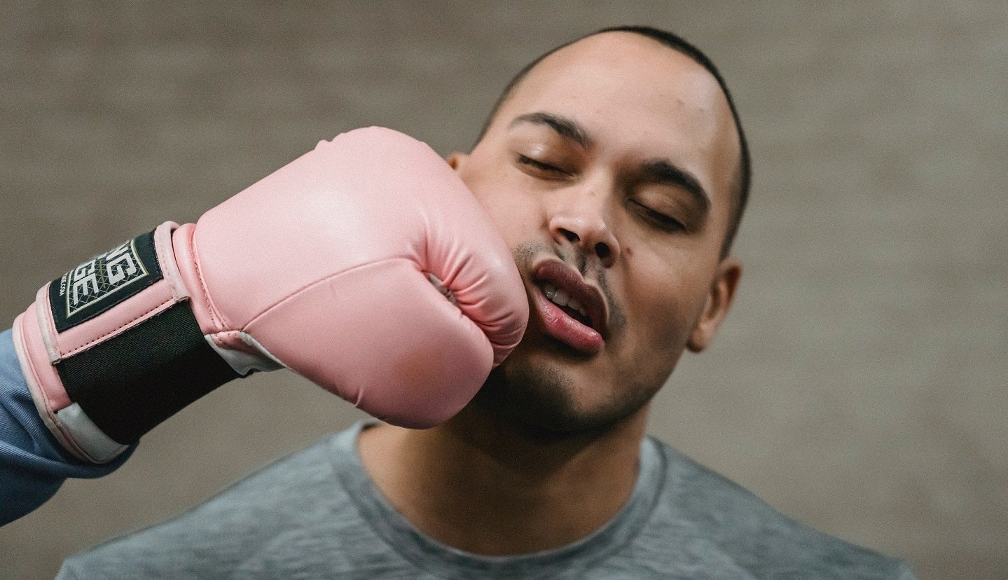 A man getting hit in the face by a pink boxing glove coming from out of frame