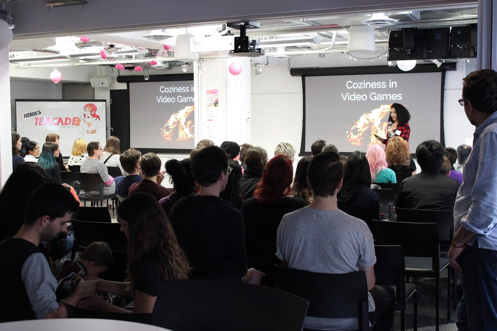 A woman gives a presentation on "Coziness in Video Games" to a crowded room at a Pixelles event