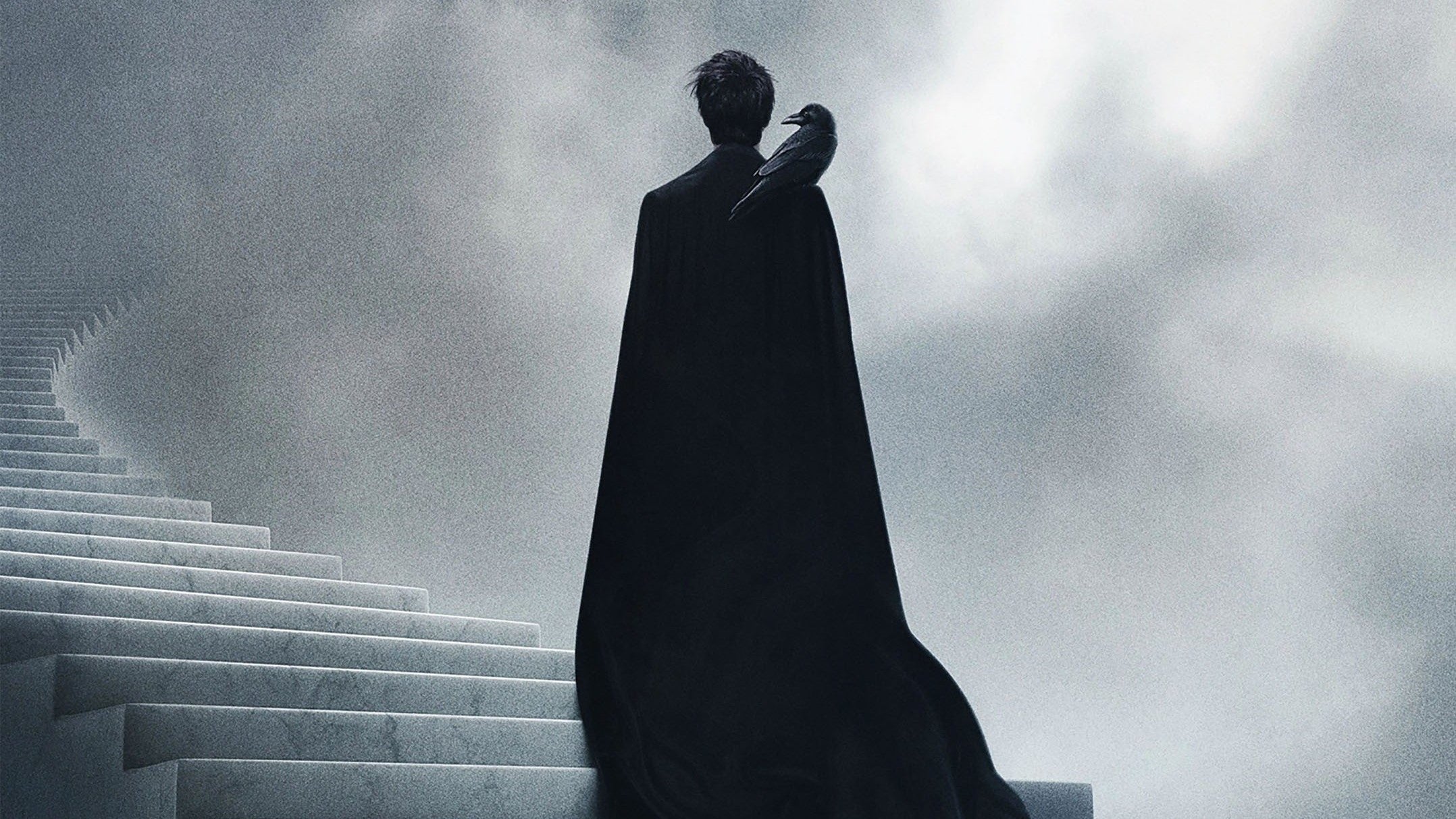 A promotional image for the Netflix Sandman series. The character Dream stands on a staircase that spirals into the clouds, back turned, with a raven on his shoulder. He is dressed, as always, all in black.