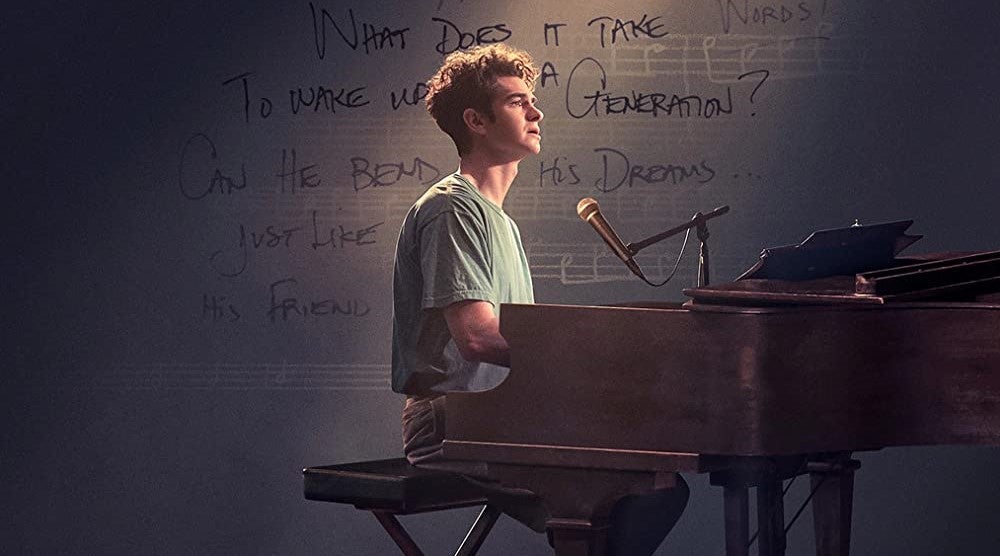 Cropped promotional image featuring Andrew Garfield as Jonathan Larson at a piano with lyrics in the background