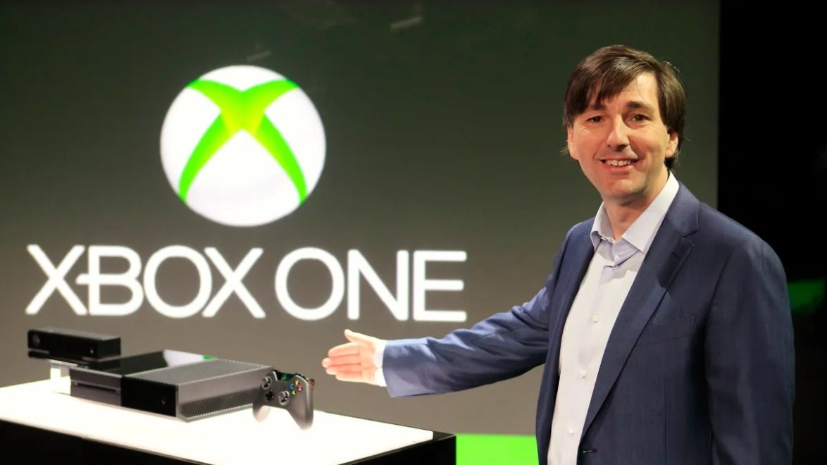 Former Xbox head Don Mattrick gestures toward an Xbox One in the background in a pre-launch press photo